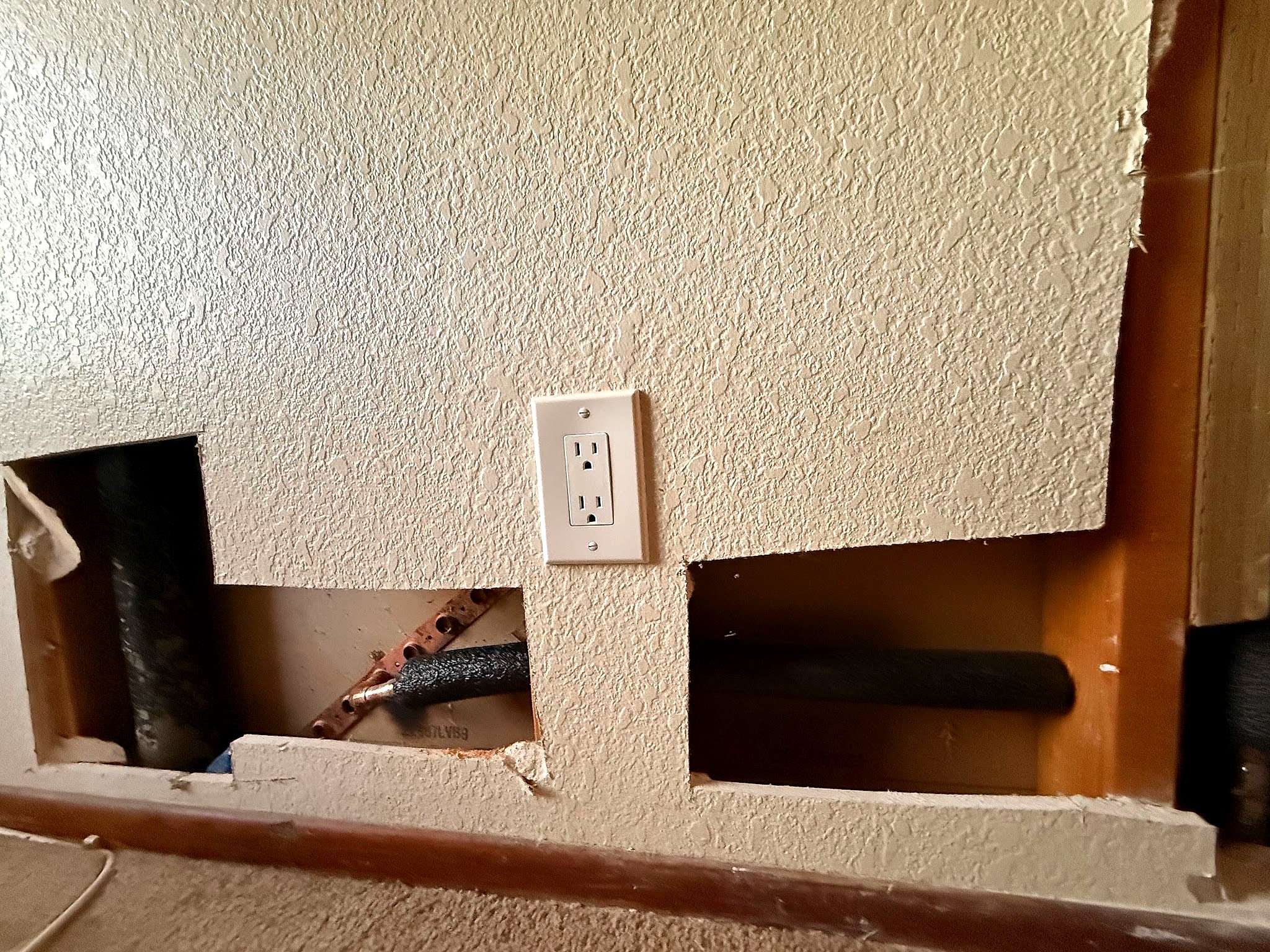 Drywall cut open along the baseboard to reroute a pipe